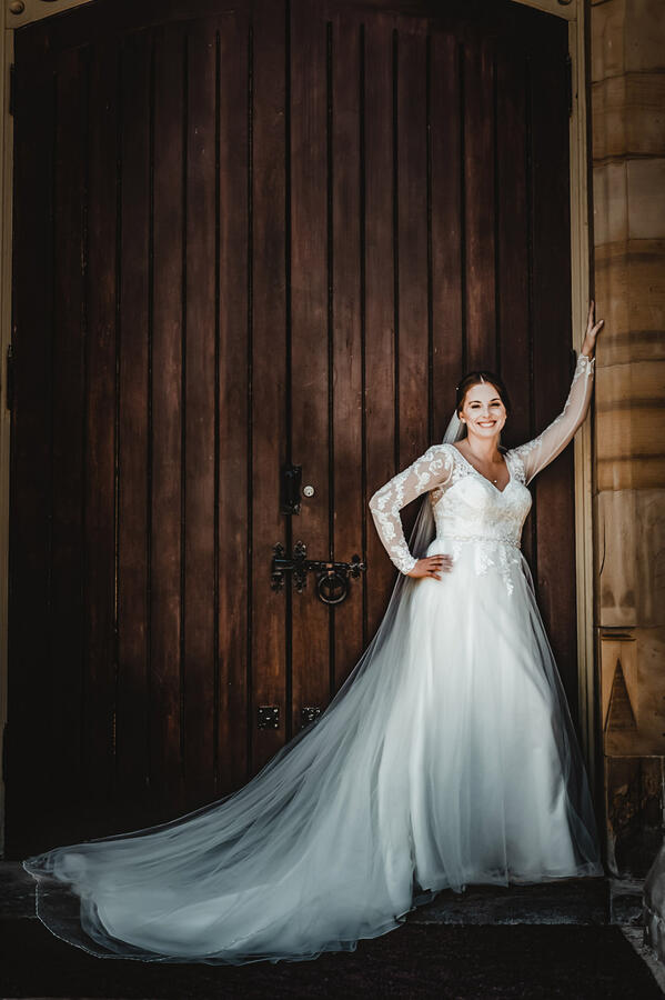 Bride with arm up against an old doorframe, smiling at camera
