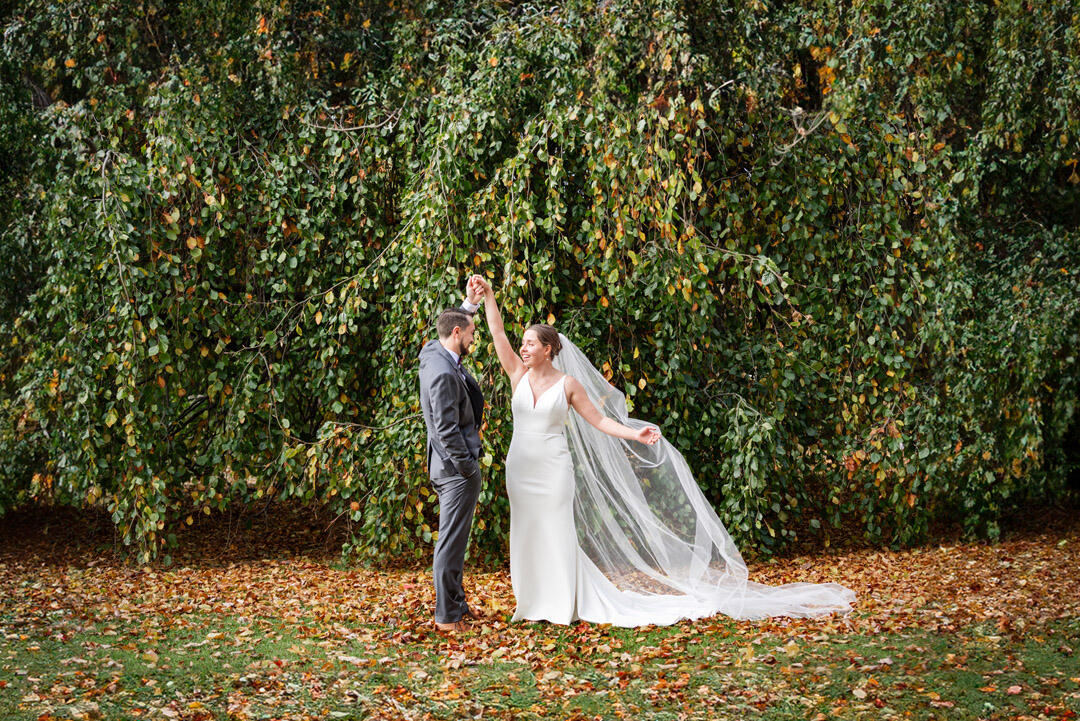 Groom twirling bride in front of a wall of greenery