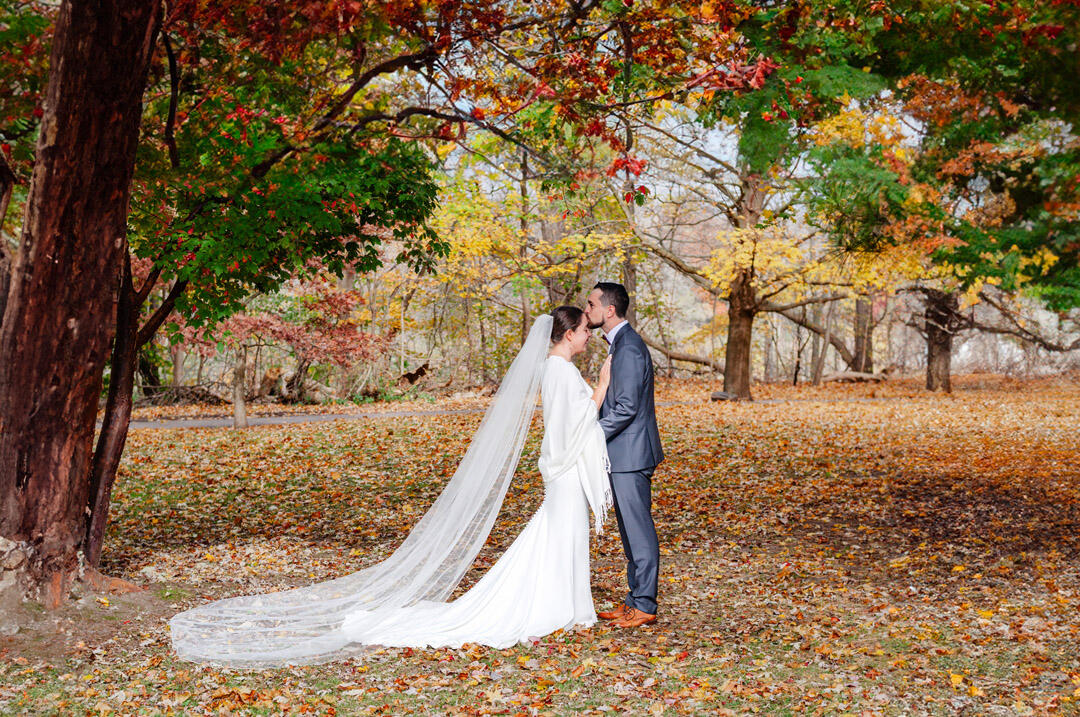 Groom kissing Bride's forehead with autumn leaves surrounding them