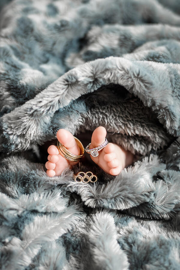 Baby - newborn toes surrounded by blanket, with wedding rings + olympic ring on toes