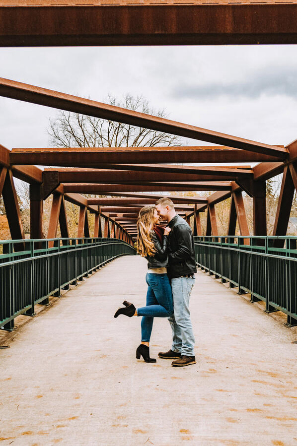 Couple - standing on a bridge, snuggling up to one another, with a foot pop