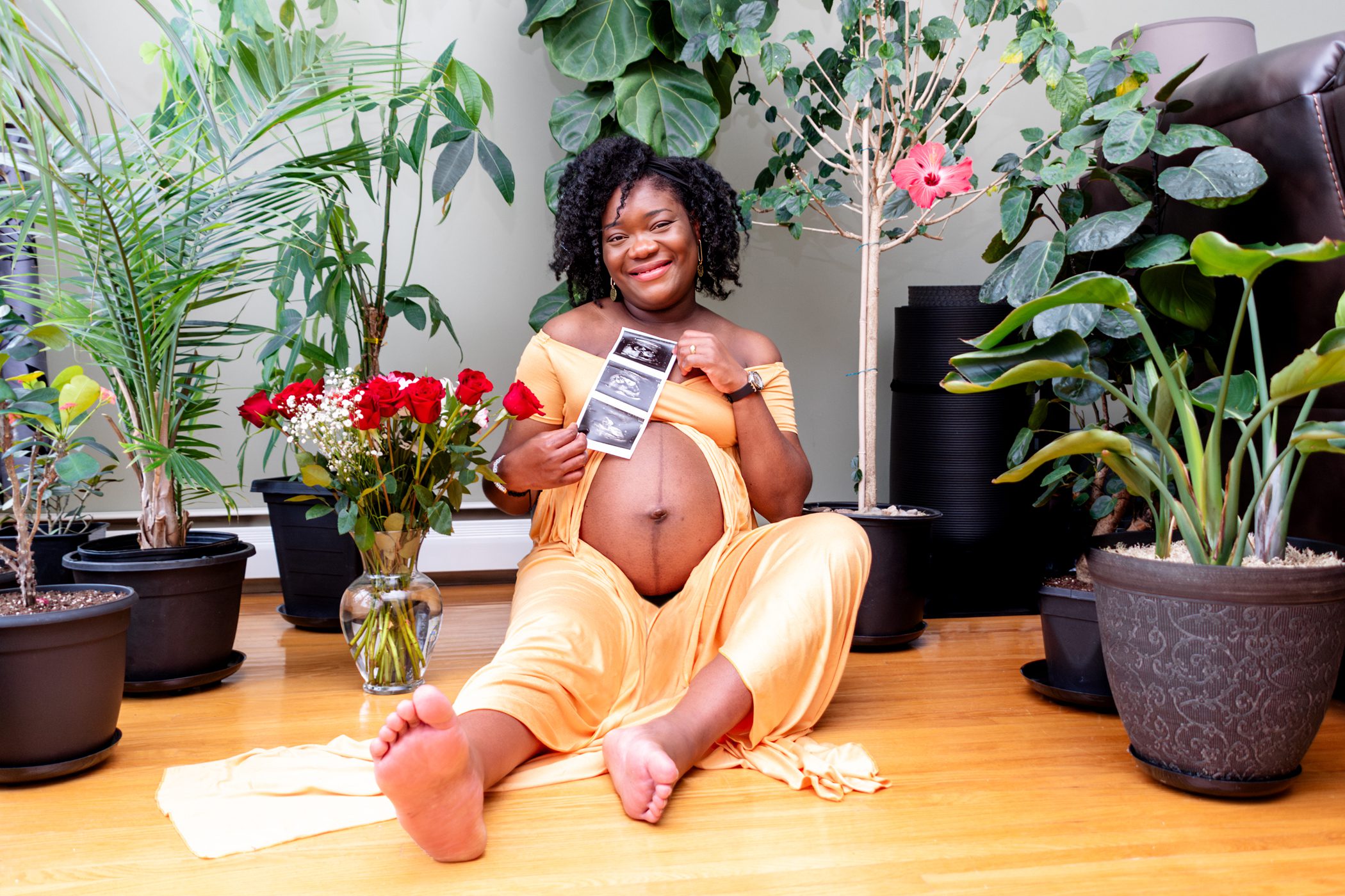 Maternity mom sitting on the floor, holding sonogram, surrounded by plants
